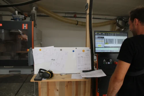 Florian steht am CNC-Steurpult und bereitet den nächsten Arbeitsschritt vor