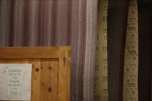 Nahaufnahme in unserer Werkstatt: Im Vordergrund eine Massive Schranktür mit einem angebrachten Zitat-Schild über Mut und Konsequenz. Im Hintergrund hängen mehrere breite Schleifbänder für eine Breitbandschleifmaschine in verschiedenen Körnungen.